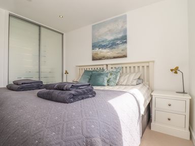 A bedroom with a double bed folded towels on it bedside table with lamp and sliding closet doors at 8 Cribbar in Newquay
