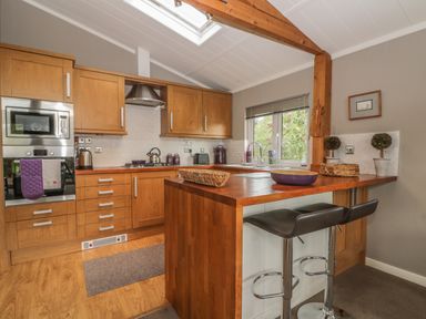 A kitchen with wooden cabinets a wooden island with two black stools and a window at Bulmer Farm Lodge in Malton