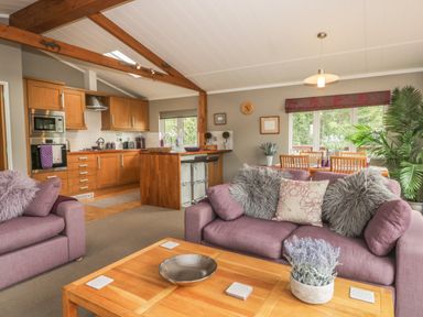 An open living room and kitchen area with purple sofas wooden cabinets and a dining table at Bulmer Farm Lodge in Malton
