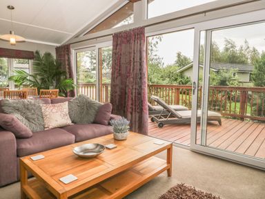 A living room with a sofa cushions and a wooden coffee table next to a sliding glass door leading to a deck with lounge chairs at Bulmer Farm Lodge in Malton