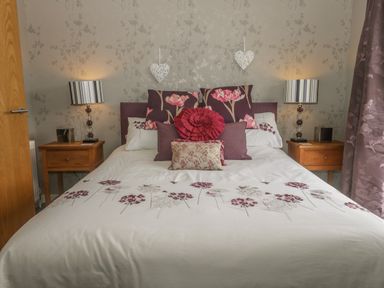 A bedroom with a bed with patterned pillows bedside tables with lamps and floral wallpaper at Bulmer Farm Lodge in Malton