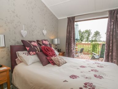 A bedroom with a bed and floral pillows and an open door leading to a balcony with chairs at Bulmer Farm Lodge in Malton