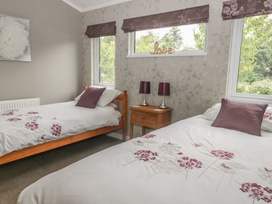 A bedroom with two single beds a wooden nightstand with two lamps and windows with blinds at Bulmer Farm Lodge in Malton