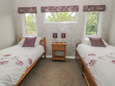 A bedroom with two single beds a wooden nightstand with two purple lamps and three windows at Bulmer Farm Lodge in Malton