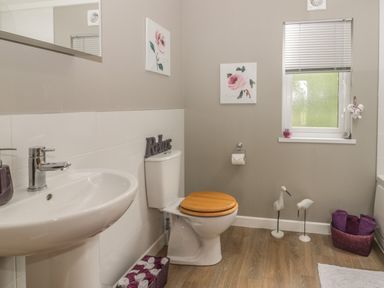 A bathroom with a sink toilet with wooden seat basket of towels and window at Bulmer Farm Lodge in Malton