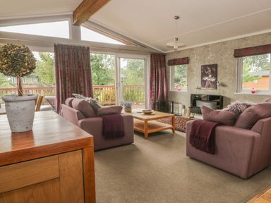 A living room with two sofas a wooden coffee table large windows and sliding glass door at Bulmer Farm Lodge in Malton