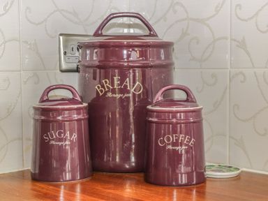 Three maroon storage jars labeled bread sugar and coffee on a wooden countertop with tiled backsplash