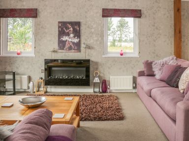 A living room with a pink sofa a wooden coffee table and two windows at Bulmer Farm Lodge in Malton
