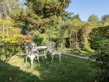 A garden with white metal table and chairs on grass surrounded by trees and plants at Woodlands Cottage in Docklow near Leominster