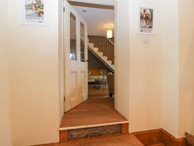 A hallway with an open door leading to a living room with a staircase and sofa at Woodlands Cottage in Docklow near Leominster