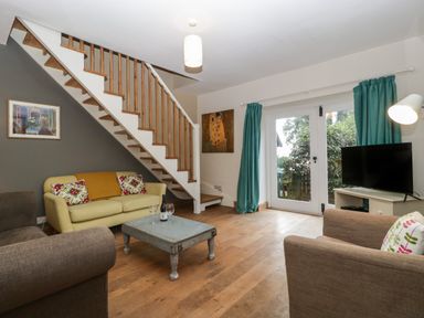 A living room with staircase yellow sofa wooden coffee table and television at Woodlands Cottage in Docklow near Leominster