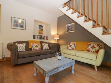 A living room with two sofas a wooden coffee table and staircase at Woodlands Cottage in Docklow near Leominster