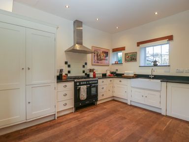 A kitchen with white cabinets a black stove wooden floor and two windows at Woodlands Cottage in Docklow near Leominster