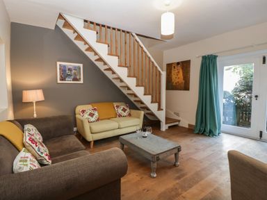 A living room with sofas and a coffee table under stairs near glass doors with curtains at Woodlands Cottage Docklow near Leominster
