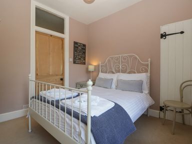 A bedroom with a double bed bedside table lamp wooden doors and a chair at Woodlands Cottage Docklow near Leominster