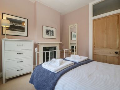 A bedroom with a bed folded towels on a blue blanket a white chest of drawers a lamp two framed pictures a mirror and a wooden door at Woodlands Cottage in Docklow near Leominster