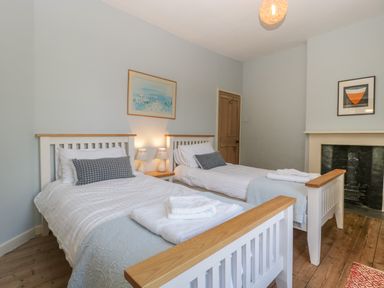 A bedroom with two single beds a small table with lamps a fireplace and artwork on the walls at Woodlands Cottage in Docklow near Leominster