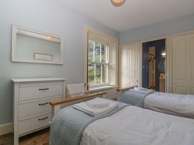 A bedroom with two single beds a dresser a window and an en suite bathroom at Woodlands Cottage in Docklow near Leominster