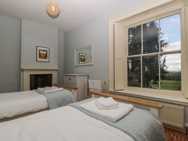 A bedroom with two single beds with towels on them a window showing outside and a fireplace at Woodlands Cottage in Docklow near Leominster