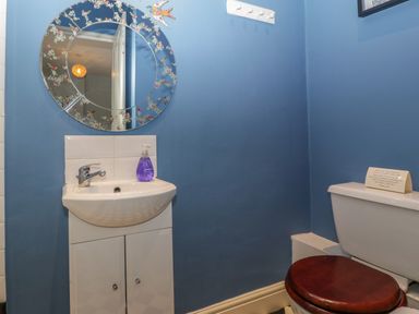 A bathroom with a white sink cabinet a round mirror soap dispenser and a toilet with a wooden seat at Woodlands Cottage in Docklow near Leominster