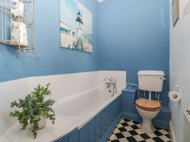 A bathroom with a bathtub a toilet a plant on a tiled ledge and a framed picture of a lighthouse on the wall at Woodlands Cottage Docklow near Leominster