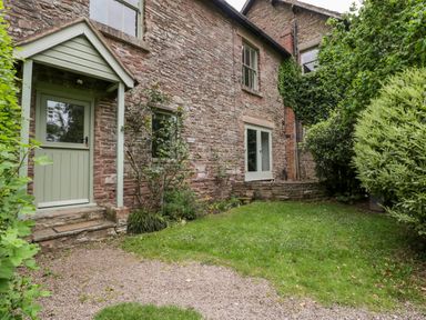 Stone cottage exterior with green door and windows garden area with grass and bushes at Woodlands Cottage in Docklow near Leominster