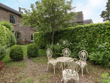 A garden with a round metal table and four chairs surrounded by bushes and a tree at Woodlands Cottage in Docklow near Leominster