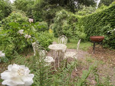An outdoor garden area with a metal table and four chairs surrounded by greenery at Woodlands Cottage in Docklow near Leominster