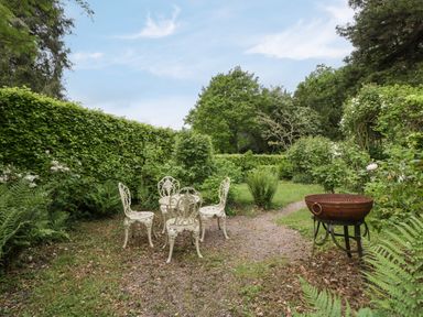 A garden with white metal table and chairs and a round barbecue grill at Woodlands Cottage in Docklow near Leominster
