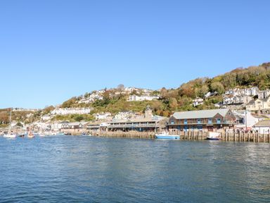 A harbor with boats and buildings along the shoreline with a hillside of houses in the background at Elmbank in Looe
