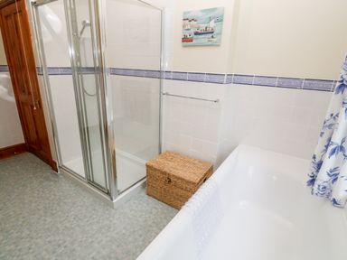 A bathroom with a glass shower enclosure a bathtub with a white mat a wicker basket and a wooden door at Elmbank in Looe