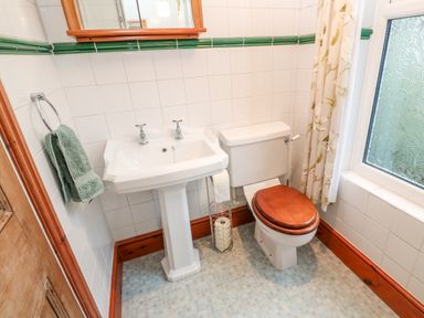 A bathroom with a pedestal sink wooden toilet seat towel rack and frosted window at Elmbank in Looe