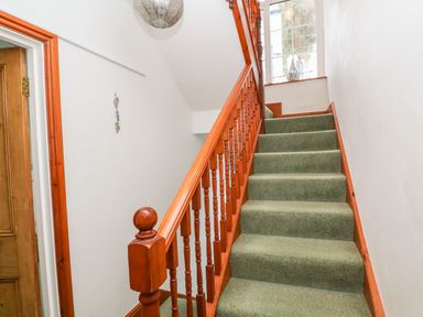 A staircase with green carpet and wooden railing next to a window at Elmbank in Looe