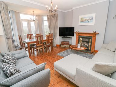 A living room with two sofas a wooden dining table and chairs a fireplace and a wall mounted TV at Elmbank in Looe