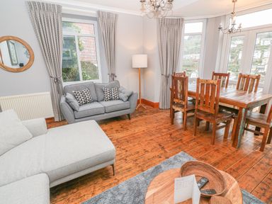 A living room with a grey sofa and wooden dining table with chairs at Elmbank in Looe