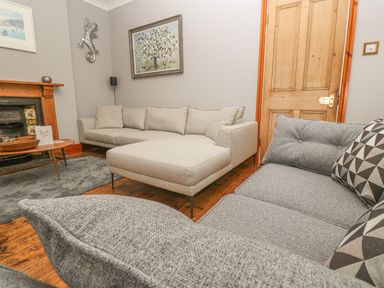 A living room with two sofas a wooden door a wooden fireplace and paintings on the wall at Elmbank in Looe