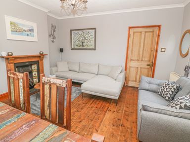 A living room with two grey sofas a wooden dining table and chairs a fireplace and wooden door at Elmbank in Looe
