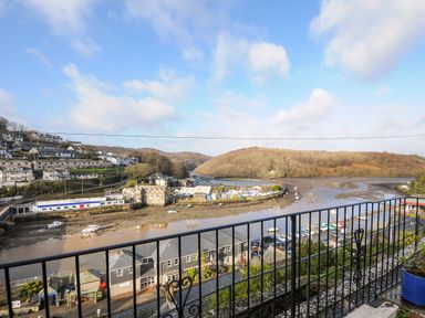 A view of a river with boats parked along the shore and houses on the hillside at Elmbank in Looe