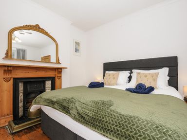 A bedroom with a bed, pillows, green blanket, wooden fireplace with a mirror above it at Elmbank in Looe