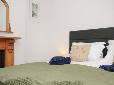 A bedroom with a bed with green blanket and decorative pillows next to a wooden fireplace and a framed picture on the wall at Elmbank in Looe