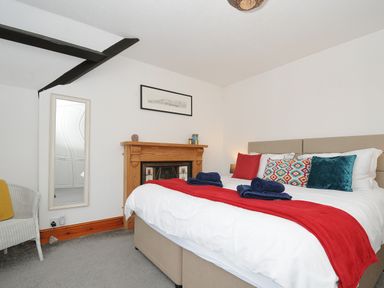 A bedroom with a bed with cushions and a red throw a wooden fireplace a mirror and a chair at Elmbank in Looe