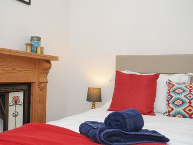 A bedroom with a bed with red and patterned cushions a rolled towel on the bed a wooden mantelpiece and a small lamp at Elmbank in Looe