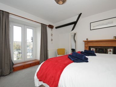 A bedroom with a bed covered with white and red bedding and blue towels by a fireplace and French doors with curtains at Elmbank in Looe