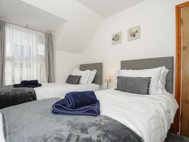 A bedroom with two single beds grey headboards white bedding grey pillows folded towels on the beds and curtains at Elmbank in Looe