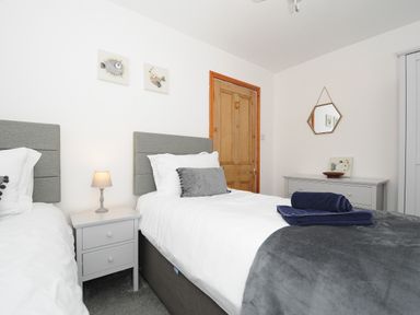 A bedroom with two single beds a grey nightstand a wooden door and a grey dresser at Elmbank in Looe
