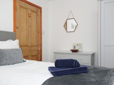 A bedroom with a bed with towels on it a wooden door a dresser with a bowl and artwork and a hexagonal mirror on the wall at Elmbank in Looe
