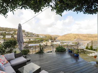 A patio with outdoor seating plants and umbrella overlooking a river and hillside at Elmbank in Looe