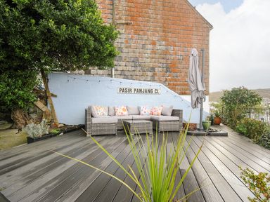 An outdoor patio with a sectional sofa with cushions and pillows a folded umbrella and plants at Elmbank in Looe