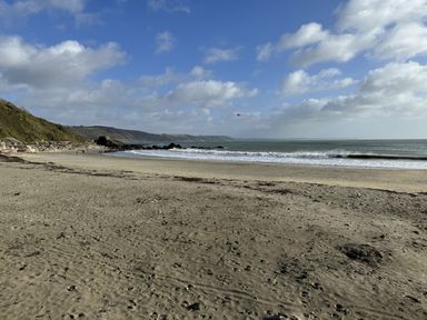 A beach with sand sea waves and hills in the background at Elmbank in Looe