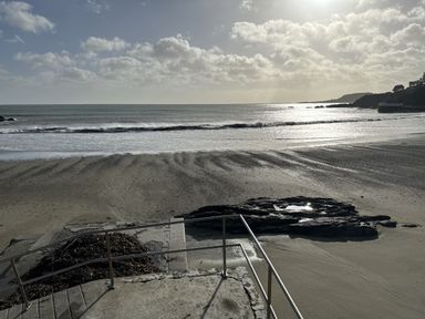 A sandy beach with waves and a concrete platform with metal railings at Elmbank in Looe
